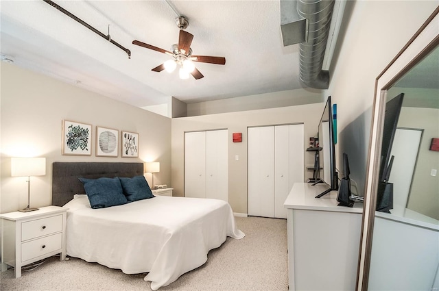bedroom featuring two closets, light carpet, and a ceiling fan