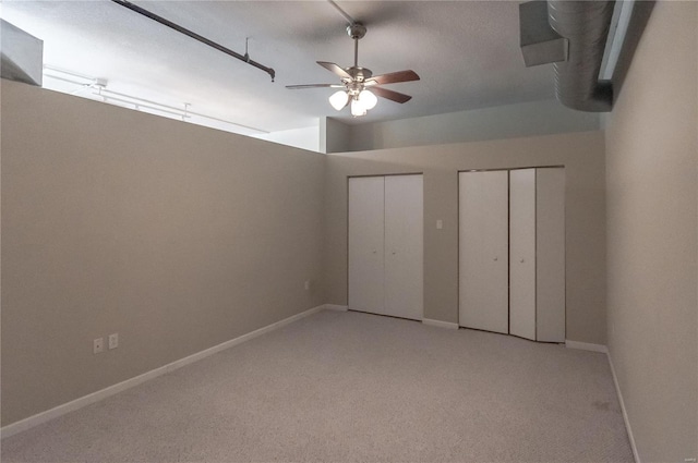 unfurnished bedroom with two closets, light colored carpet, baseboards, and a ceiling fan
