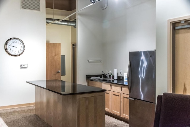kitchen with freestanding refrigerator, a sink, dark countertops, and carpet flooring