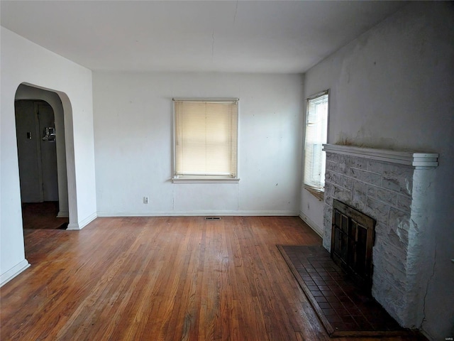 700 Pershing St E, St Louis, IL 62203 - unfurnished living room featuring arched walkways, wood finished floors, a glass covered fireplace, and baseboards
