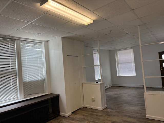 empty room featuring dark wood-style floors, a paneled ceiling, and baseboards