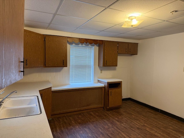kitchen with a sink, dark wood-style flooring, light countertops, and a paneled ceiling