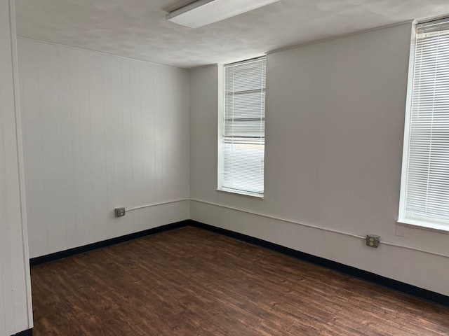 unfurnished room with dark wood-type flooring, baseboards, and healthy amount of natural light