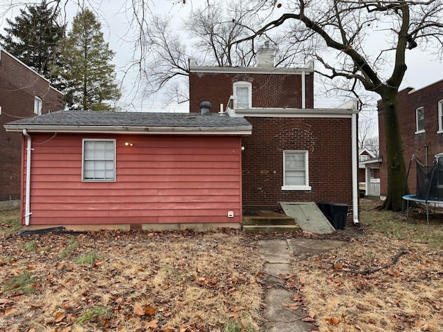 rear view of property featuring a trampoline, a chimney, and brick siding