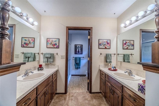 full bathroom with two vanities, baseboards, and a textured ceiling