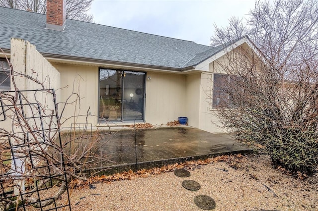 rear view of property with a shingled roof, a patio, and a chimney