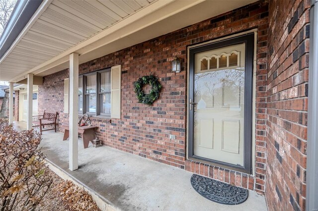 view of exterior entry with a porch and brick siding