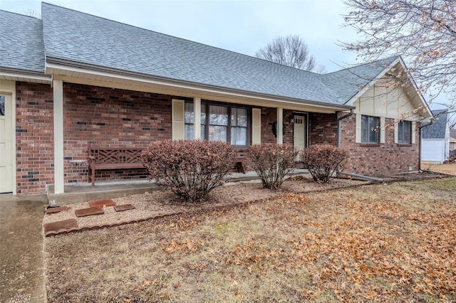 view of front of property with roof with shingles, a porch, and brick siding