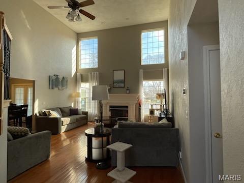 living room featuring a ceiling fan, a high ceiling, dark wood-style floors, a fireplace, and a textured wall