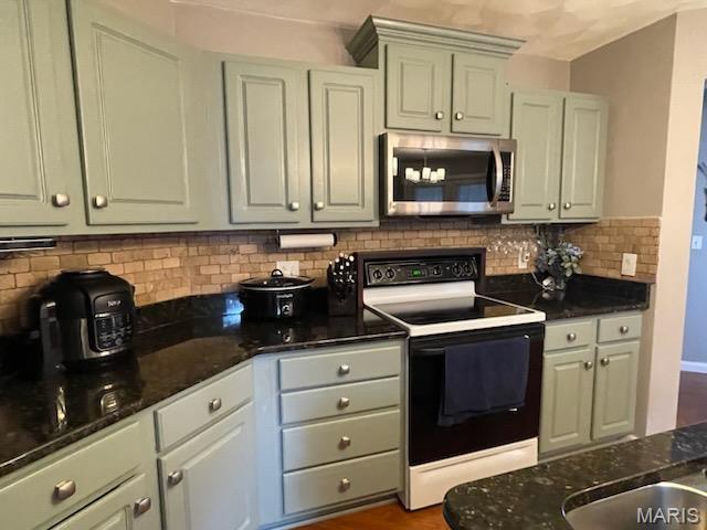 kitchen with stainless steel microwave, electric range oven, decorative backsplash, and dark stone counters