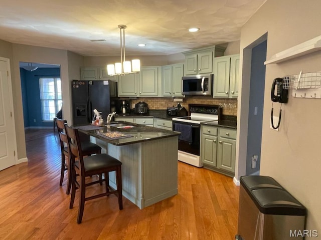 kitchen with electric range, stainless steel microwave, black fridge, dark countertops, and a breakfast bar area