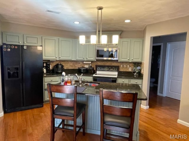 kitchen featuring black fridge with ice dispenser, stainless steel microwave, electric range, a sink, and dark countertops