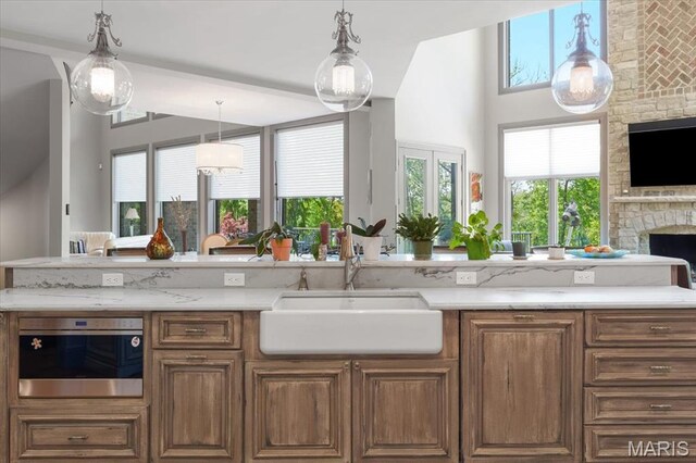 2535 S Lindbergh Blvd, Saint Louis, MO 63131 - kitchen featuring a sink, a stone fireplace, stainless steel oven, open floor plan, and brown cabinetry
