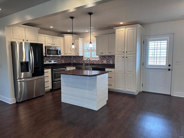 kitchen with appliances with stainless steel finishes, dark wood-style flooring, dark countertops, white cabinetry, and tasteful backsplash