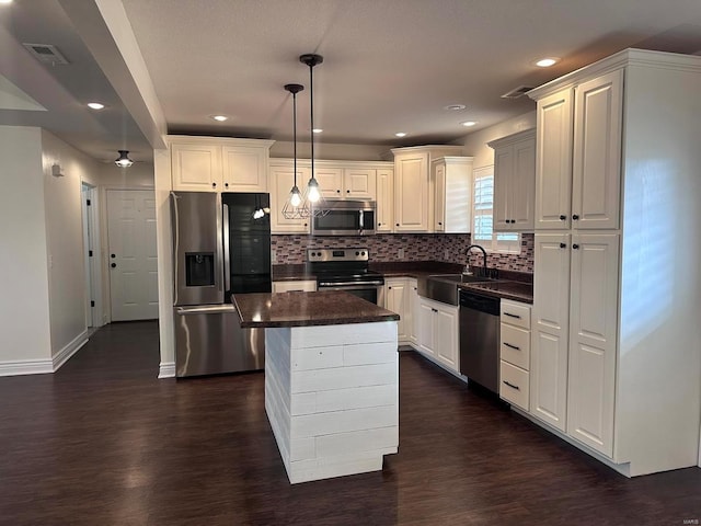 kitchen with appliances with stainless steel finishes, a sink, dark countertops, tasteful backsplash, and dark wood-style floors