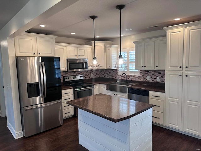 kitchen with appliances with stainless steel finishes, a sink, dark countertops, dark wood-style floors, and white cabinetry