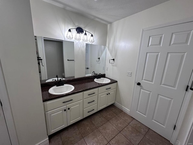 bathroom featuring double vanity, a textured ceiling, toilet, tile patterned floors, and baseboards