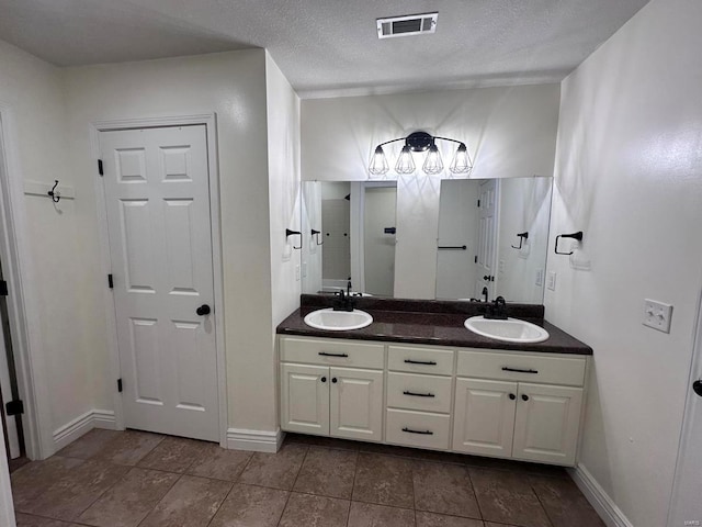 full bathroom featuring double vanity, tile patterned flooring, baseboards, and a textured ceiling