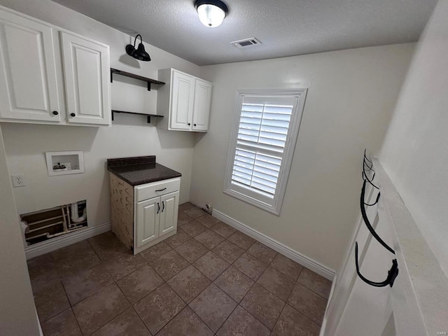 clothes washing area with hookup for a washing machine, cabinet space, a textured ceiling, and baseboards