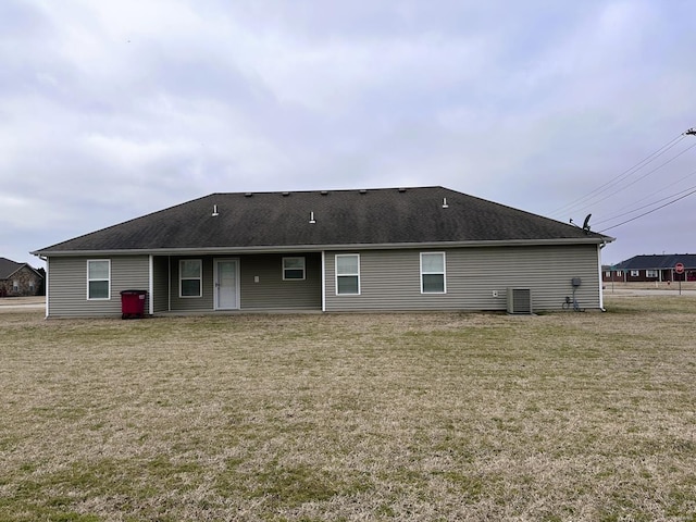 rear view of property featuring a yard, central AC unit, and a shingled roof