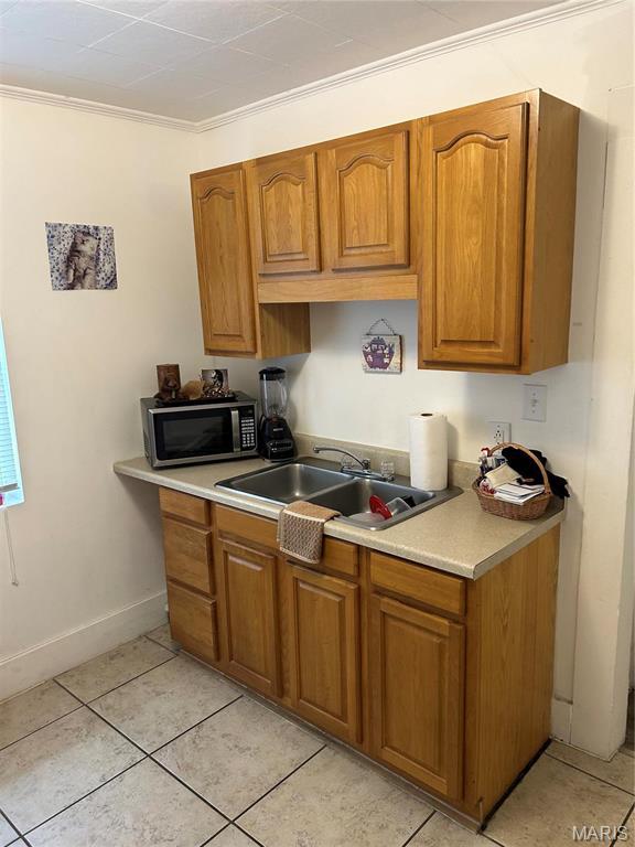 618 Church St, Hannibal, MO 63401 - kitchen with stainless steel microwave, brown cabinets, light countertops, light tile patterned flooring, and ornamental molding