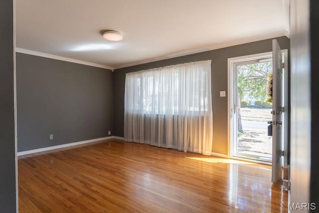 spare room featuring wood finished floors, crown molding, and baseboards
