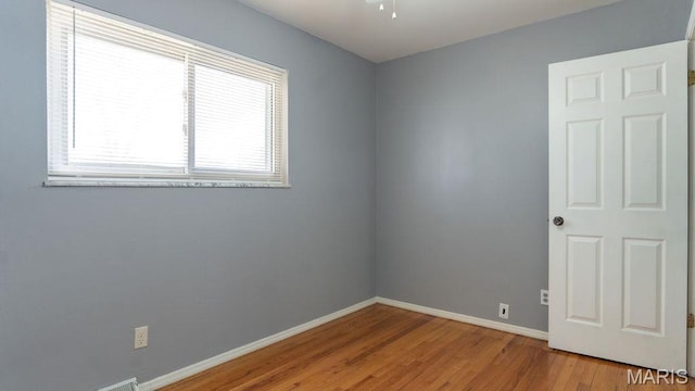 unfurnished room featuring plenty of natural light, wood finished floors, and baseboards
