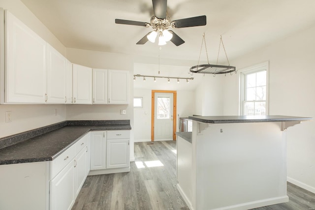 204 S Railroad St, Medora, IL 62063 - kitchen with dark countertops, light wood-style floors, a ceiling fan, a kitchen bar, and white cabinetry