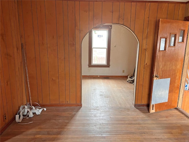 spare room featuring arched walkways, wooden walls, and hardwood / wood-style floors