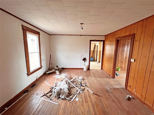 empty room featuring light wood-type flooring, ornamental molding, baseboards, and wood walls