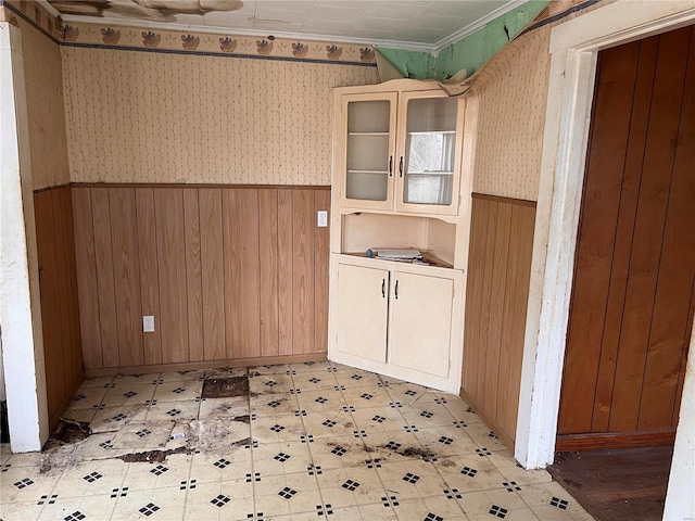 unfurnished dining area featuring wainscoting, wood walls, wallpapered walls, and light floors