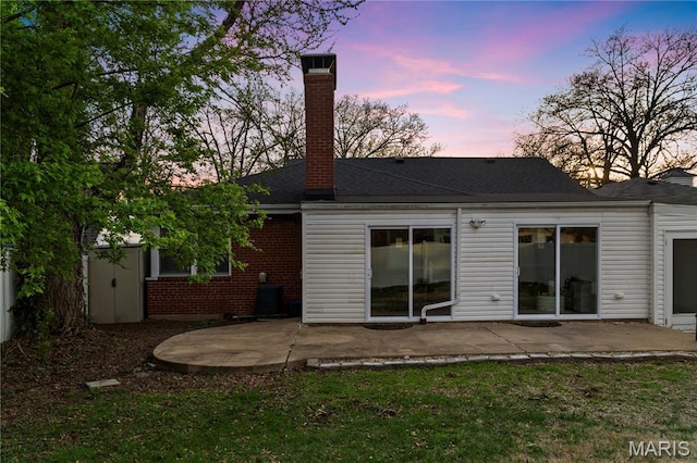 5816 Jamieson Ave, Saint Louis, MO 63109 - back of property at dusk with a patio, a chimney, brick siding, and roof with shingles