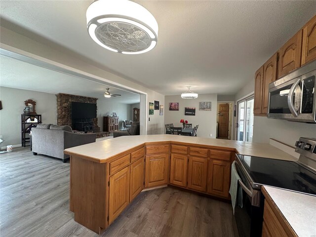 kitchen featuring appliances with stainless steel finishes, light countertops, wood finished floors, a peninsula, and a ceiling fan