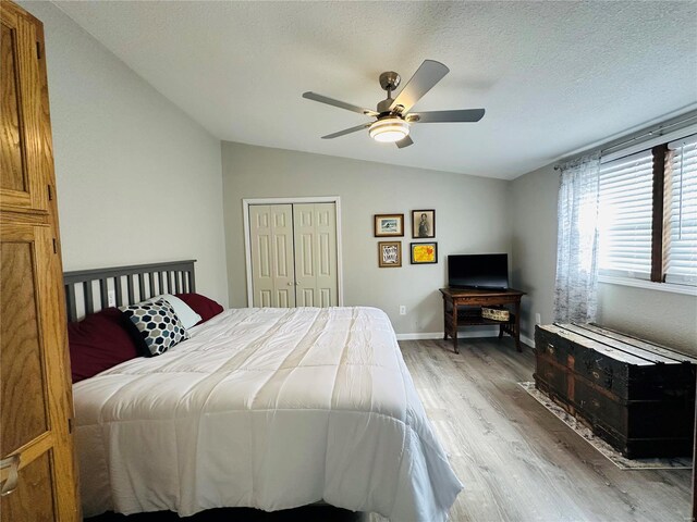 bedroom with light wood-style flooring, vaulted ceiling, a closet, ceiling fan, and a textured ceiling