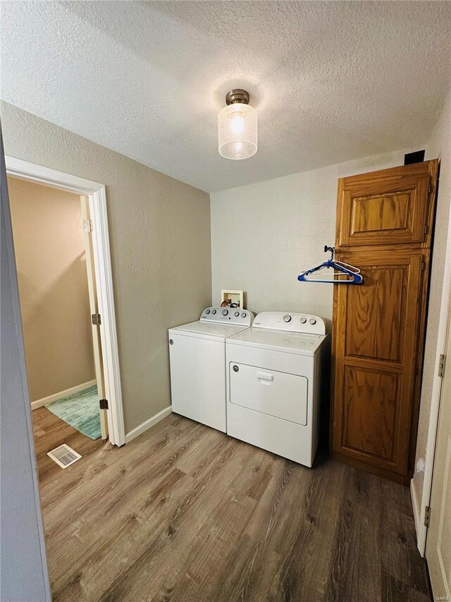 clothes washing area featuring wood finished floors, washer and clothes dryer, a textured ceiling, and baseboards