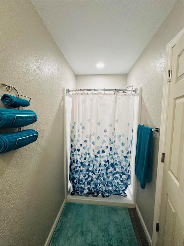 bathroom featuring a textured wall, a shower with curtain, and baseboards