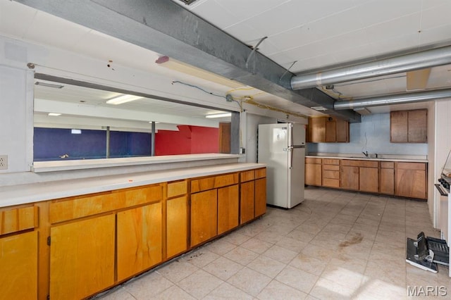 209 S Montgomery St, Gillespie, IL 62033 - kitchen with freestanding refrigerator, light countertops, a sink, and brown cabinetry