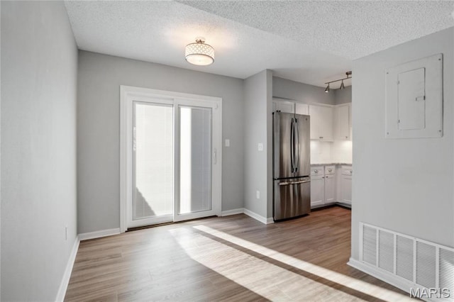 1508 Swallow Dr, Saint Louis, MO 63144 - kitchen with freestanding refrigerator, electric panel, white cabinetry, wood finished floors, and a textured ceiling