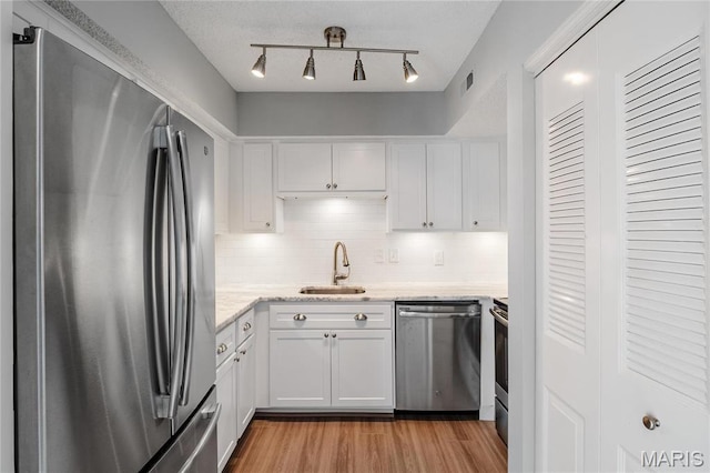 1508 Swallow Dr, Saint Louis, MO 63144 - kitchen featuring stainless steel appliances, a sink, white cabinetry, light wood finished floors, and backsplash