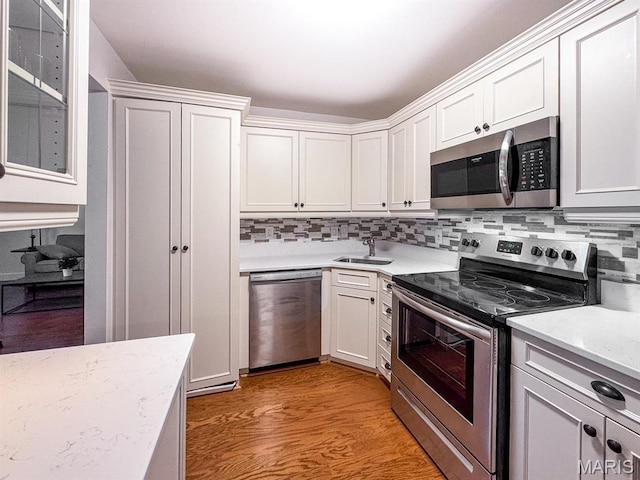 kitchen with stainless steel appliances, decorative backsplash, a sink, white cabinetry, and light wood-type flooring