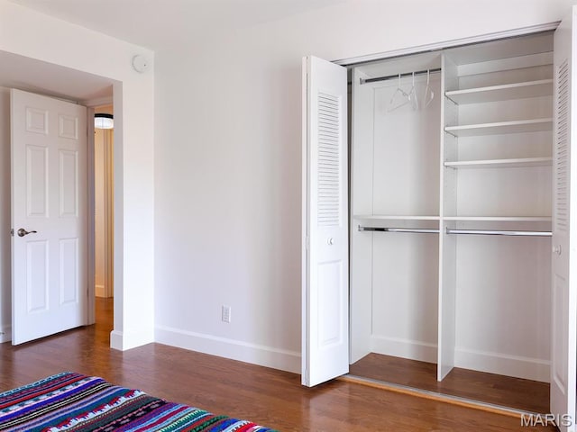 unfurnished bedroom with baseboards, wood finished floors, and a closet