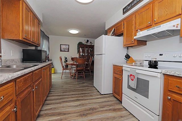 918 Susan St, Dexter, MO 63841 - kitchen with white appliances, under cabinet range hood, brown cabinets, wood finished floors, and a textured ceiling