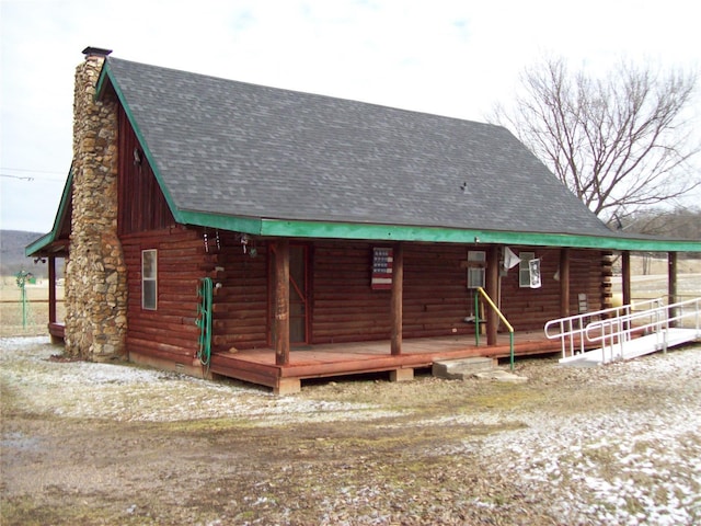 view of front of house with log siding, a shingled roof, a chimney, and covered porch