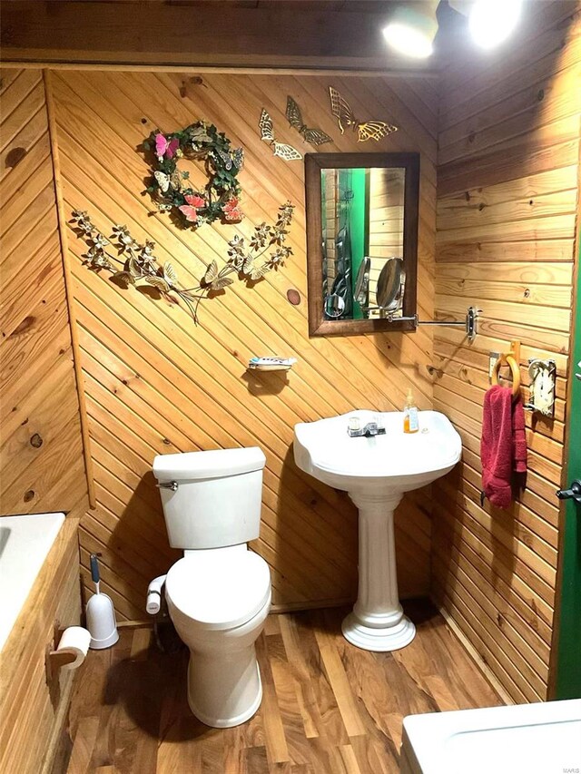 bathroom with wood finished floors, wood walls, and toilet