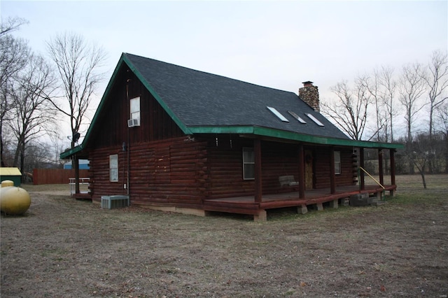 view of side of home with log exterior, a porch, a shingled roof, a chimney, and cooling unit