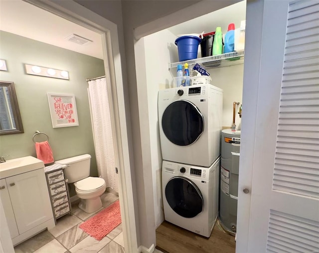 clothes washing area with stacked washing machine and dryer and water heater