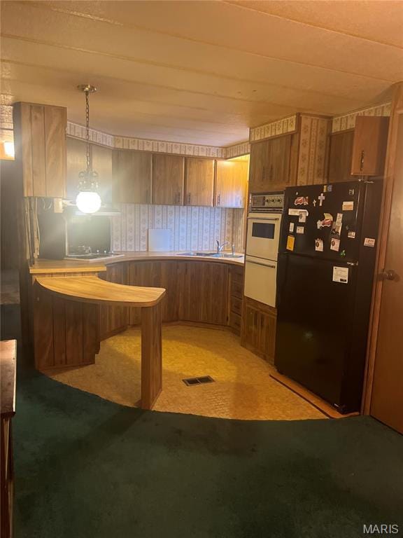 kitchen with freestanding refrigerator, brown cabinets, light colored carpet, light countertops, and pendant lighting
