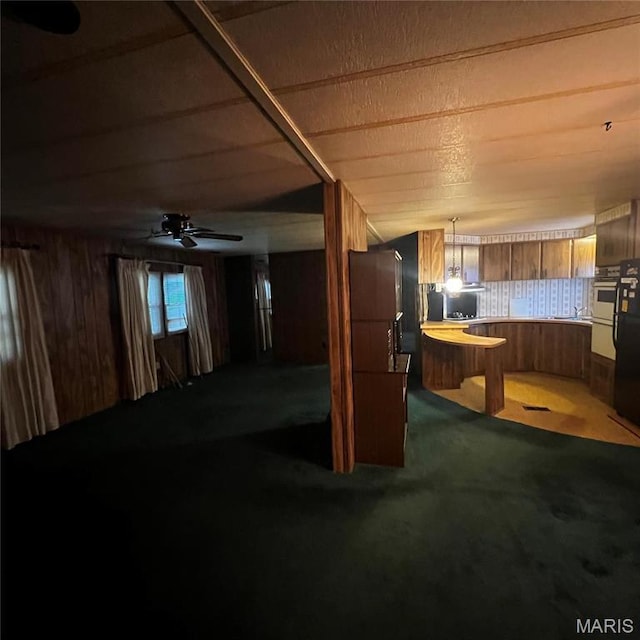 below grade area with carpet floors, wood walls, refrigerator, and a ceiling fan