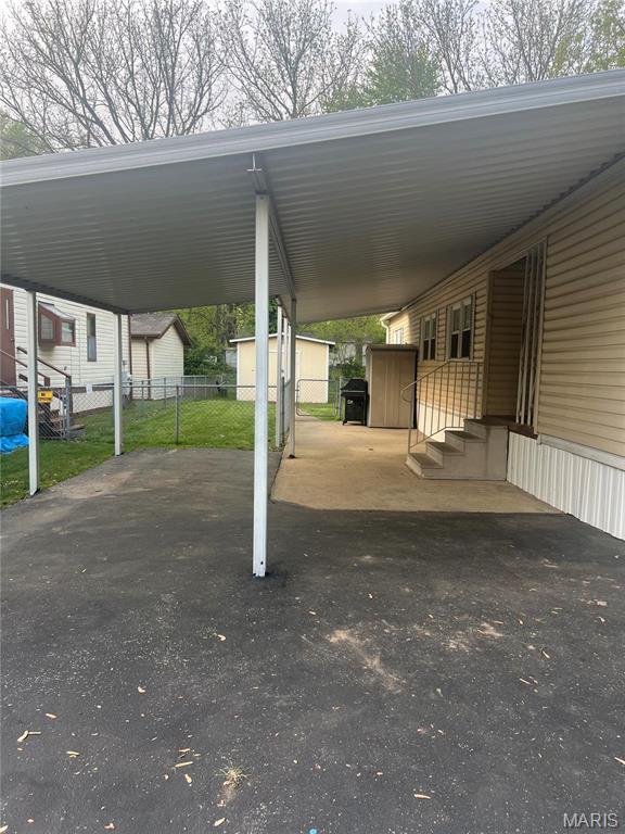 view of vehicle parking featuring a storage unit, fence, entry steps, and an attached carport