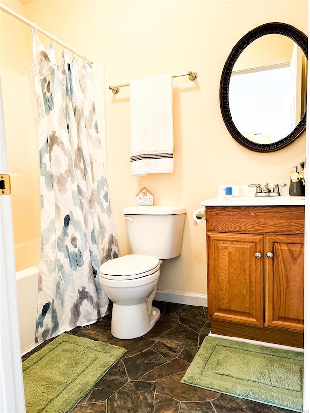 bathroom featuring toilet, baseboards, vanity, stone finish flooring, and shower / bath combination with curtain